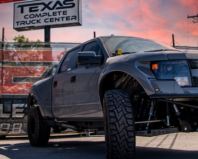 Gray truck in front of Texas Complete Truck Center signs with a colorful sky.